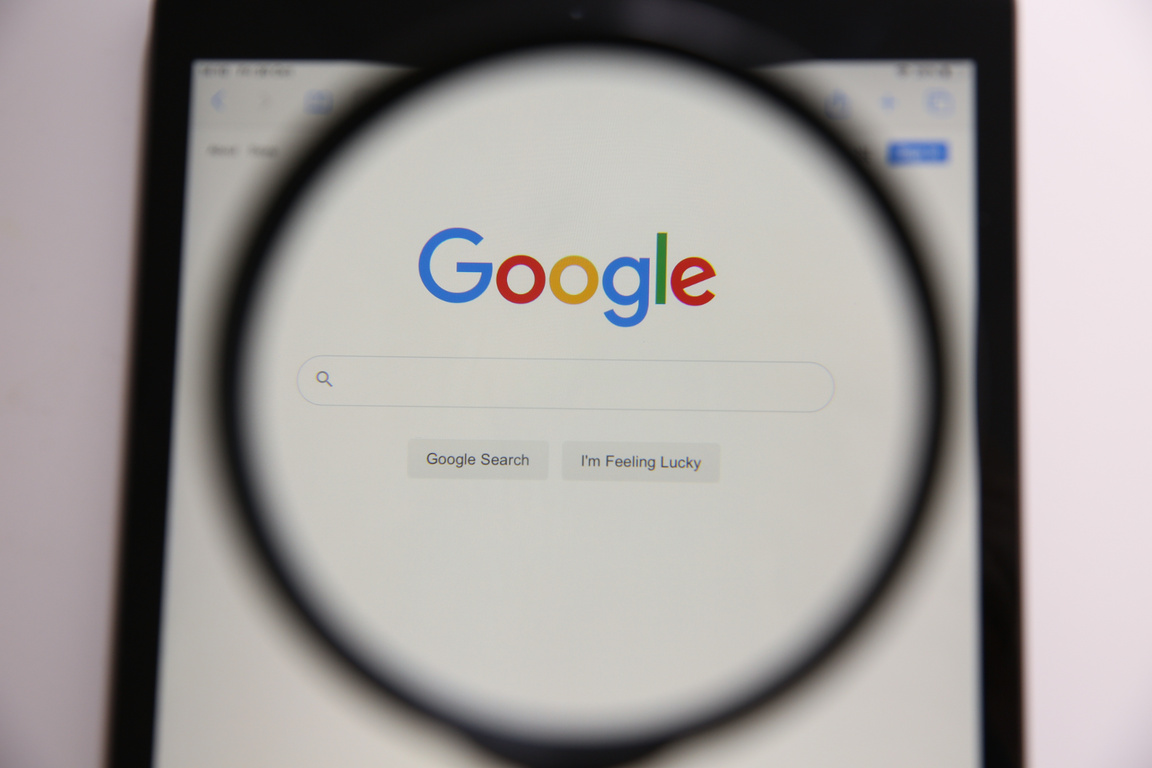 MYKOLAIV, UKRAINE - OCTOBER 30, 2020: Looking through Magnifying Glass at Screen with Google Search Bar on White Background